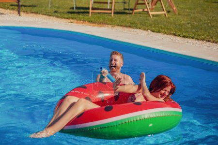 Téléchargez les photos : Beau jeune couple amoureux s'amuser à nager et éclabousser d'eau l'un sur l'autre dans la piscine, se détendre pendant les vacances d'été - en image libre de droit