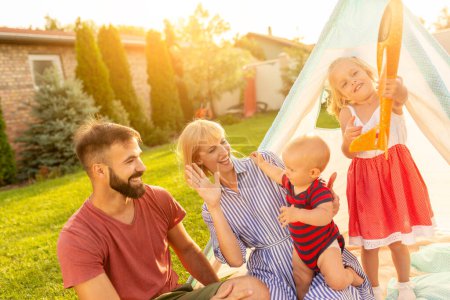 Foto de Hermosa familia feliz joven que se divierte pasar soleado día de verano acampando en el patio trasero, los padres jugando con sus hijos - Imagen libre de derechos
