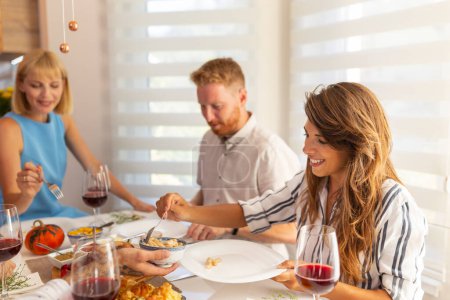 Téléchargez les photos : Groupe de jeunes amis joyeux réunis autour de la table, s'amusant tout en déjeunant ensemble à la maison - en image libre de droit