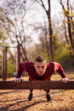 Photo for Man working out outdoors in street workout park on a sunny autumn day, doing push ups - Royalty Free Image