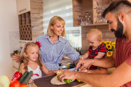 Photo for Beautiful happy family having fun cooking lunch together, mother and daughter cutting vegetables while father and son assisting and enjoying leisure time at home - Royalty Free Image