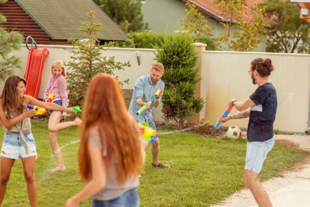 Foto de Grupo de jóvenes amigos que se divierten pasando el día de verano al aire libre, jugando con pistolas de agua, salpicándose el agua, corriendo y persiguiéndose mutuamente - Imagen libre de derechos