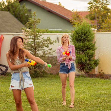 Téléchargez les photos : Groupe de jeunes amis s'amuser passer la journée d'été à l'extérieur, jouer avec des pistolets à éjaculation féminine, éclabousser de l'eau les uns sur les autres, courir et courir après les autres - en image libre de droit