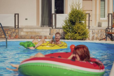 Téléchargez les photos : Beau jeune couple amoureux s'amuser à nager et éclabousser de l'eau l'un sur l'autre dans la piscine, jouer avec des pistolets à éjaculation et se détendre pendant les vacances d'été - en image libre de droit