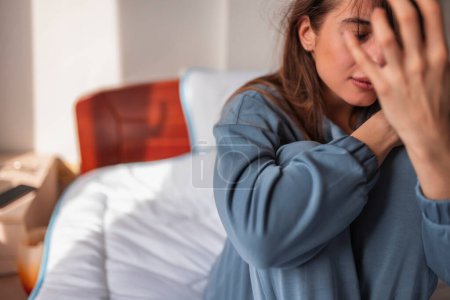 Photo for Upset young woman wearing pajamas sitting on bed in the morning, crying - Royalty Free Image