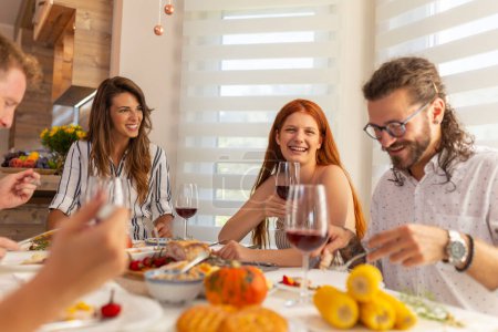 Téléchargez les photos : Groupe de jeunes amis réunis autour de la table pour Thanksgiving, célébrer et avoir traditionnel Thanksgiving dîner à la maison tous ensemble - en image libre de droit
