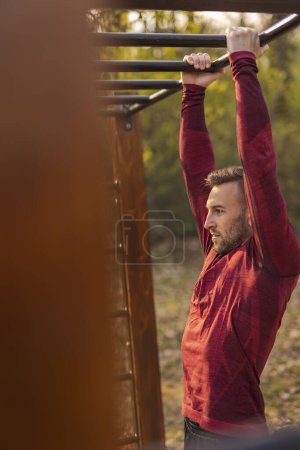 Photo for Men in sportswear doing pull ups while working out outdoors in a street workout park - Royalty Free Image