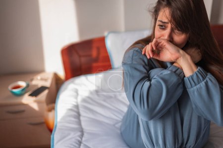 Téléchargez les photos : Jeune femme souffrant de dépression portant un pyjama assis sur le lit le matin, pleurant triste et désespérée avec enduit de maquillage - en image libre de droit