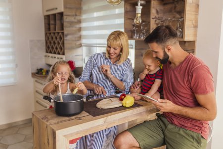 Photo for Mother and father sitting at kitchen counter and having fun cooking lunch with their children - Royalty Free Image