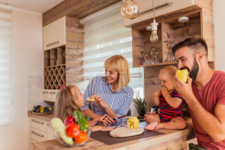 Photo for Beautiful happy parents and children having fun preparing food and cutting vegetables for lunch, enjoying leisure time together at home - Royalty Free Image