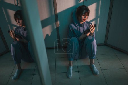 Foto de Mujer suicida deprimida sentada en el suelo en la oscuridad, sosteniendo un arma y llorando, pensando en suicidarse; mujer asustada víctima de violencia doméstica sosteniendo un arma para defensa propia - Imagen libre de derechos
