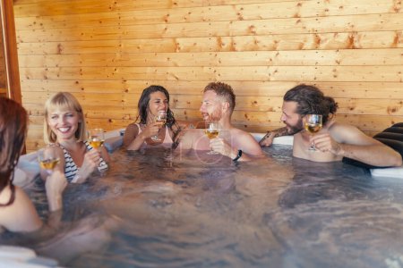 Téléchargez les photos : Groupe de jeunes amis joyeux se détendre dans un centre de spa hôtel spa bain à remous, boire du vin et s'amuser pendant les vacances - en image libre de droit