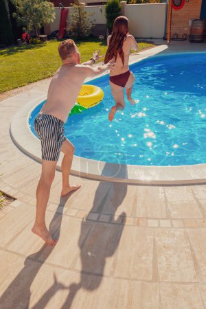 Foto de Hermosa pareja joven en el amor que se divierten saltando y empujándose unos a otros en la piscina, relajándose mientras que en unas vacaciones de verano - Imagen libre de derechos