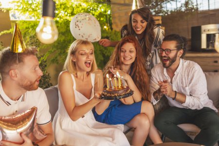 Foto de Grupo de amigos divirtiéndose en una fiesta de cumpleaños, chica de cumpleaños soplando velas de un pastel después de pedir un deseo - Imagen libre de derechos