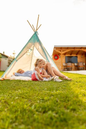 Foto de Hermosa madre e hija divirtiéndose acampando y jugando en el patio trasero, tumbado en una tienda de campaña y relajándose afuera en un día soleado de verano - Imagen libre de derechos