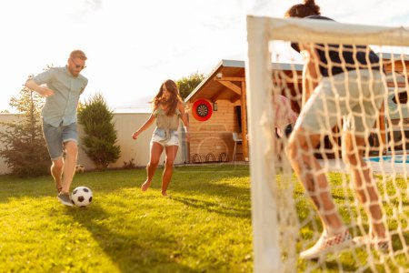 Photo for Group of young friends having fun while playing football on sunny summer day; young business team having fun while on team building trip, participating in mini football competition - Royalty Free Image