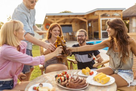 Foto de Grupo de personas divirtiéndose en la fiesta de barbacoa al lado de la piscina, haciendo un brindis con botellas de cerveza y disfrutando de días soleados de verano al aire libre - Imagen libre de derechos