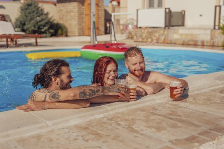 Photo for Group of cheerful young friends having fun at the swimming pool, leaning on the edge while making a toast with glasses of beer, relaxing while on a summer vacation - Royalty Free Image