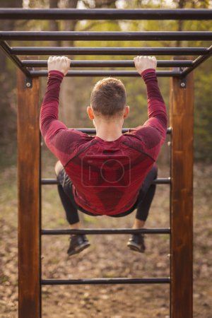 Photo for Muscular man working out on monkey bars outdoors in a street workout park - Royalty Free Image