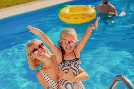 Téléchargez les photos : Vue en angle élevé de la jeune mère s'amusant à jouer avec sa fille dans la piscine, profiter d'une chaude journée d'été ensoleillée à l'extérieur et se détendre pendant ses vacances - en image libre de droit
