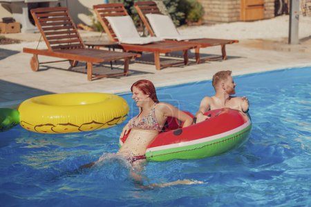 Photo for Beautiful young couple in love having fun swimming and splashing water on each other in the pool, climbing and jumping of a pool float, relaxing while on a summer vacation - Royalty Free Image