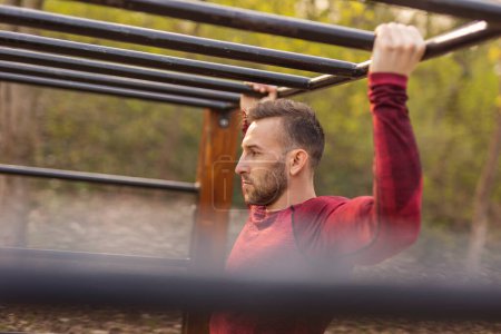Téléchargez les photos : Les hommes en vêtements de sport faisant des pull-ups tout en travaillant à l'extérieur dans un parc d'entraînement de rue - en image libre de droit