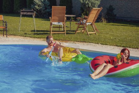 Schönes junges verliebtes Paar, das Spaß beim Schwimmen hat und sich im Pool gegenseitig mit Wasser bespritzt, während eines Sommerurlaubs entspannt