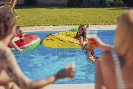 Téléchargez les photos : Groupe de jeunes amis s'amuser à la fête de piscine d'été, boire de la bière, bronzer et se détendre tout en flottant sur des matelas gonflables - en image libre de droit