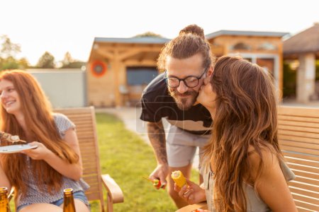 Téléchargez les photos : Beau jeune couple amoureux s'amuser avec des amis à la fête barbecue arrière-cour, embrasser et profiter des jours ensoleillés d'été en plein air - en image libre de droit