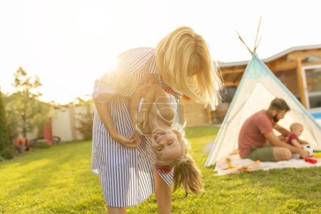 Foto de Familia feliz pasar un día acampando en su patio trasero, los padres se divierten jugando con los niños, la madre llevando y cosquillas hija mientras el padre está jugando con el niño - Imagen libre de derechos