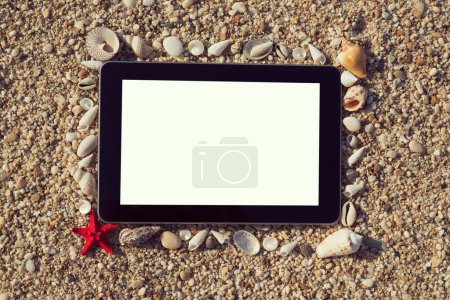 Foto de Marco de fotos hecho de conchas marinas y guijarros con dos estrellas de mar colocadas junto a él y tableta de computadora dentro del marco con pantalla en blanco en la playa - Imagen libre de derechos