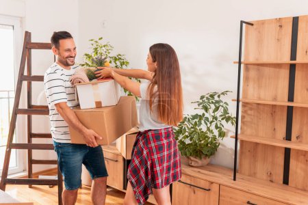 Photo for Couple in love moving in together, having fun while carrying cardboard boxes and setting up the new apartment - Royalty Free Image