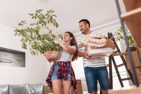 Photo for Beautiful young couple in love moving in together, having fun while carrying cardboard boxes and setting up the new apartment - Royalty Free Image