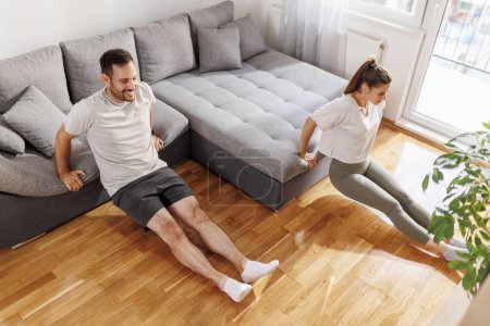 Téléchargez les photos : Couple faisant triceps plonge sur le canapé du salon tout en travaillant ensemble à la maison - en image libre de droit