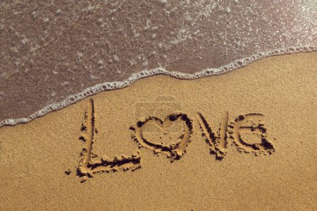 Téléchargez les photos : Mot amour écrit à la main dans le sable doré sur la plage à côté de la ligne de flottaison - en image libre de droit