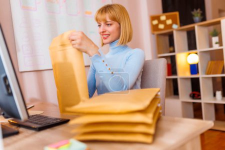 Foto de Mujer propietaria de una pequeña empresa sentada en su escritorio en la oficina en el hogar, empaquetando productos para la entrega; Empresaria mujer empaquetando pedidos en línea para envío - Imagen libre de derechos