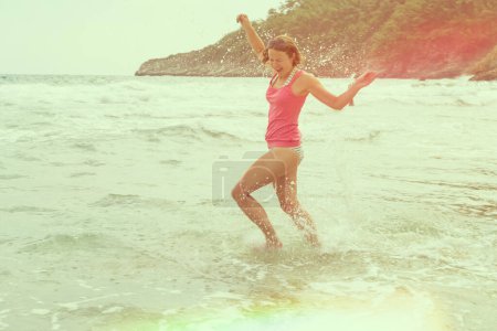 Téléchargez les photos : Jeune femme heureuse courant dans l'eau et l'éclaboussant. Plaisir et liberté pendant les vacances à la plage - en image libre de droit