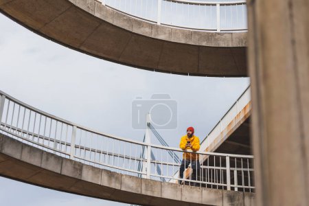 Téléchargez les photos : Homme actif debout et relaxant sur un chemin de pont tout en prenant une pause de la course du matin - en image libre de droit