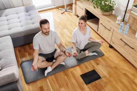 Téléchargez les photos : Vue grand angle de couple relaxant tout en faisant une séance de yoga ensemble à la maison - en image libre de droit