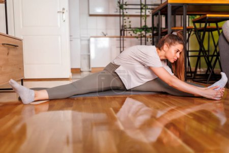 Téléchargez les photos : Vue à angle bas de la jeune femme en vêtements de sport étirant sur tapis de yoga après avoir fait de l'entraînement à la maison - en image libre de droit