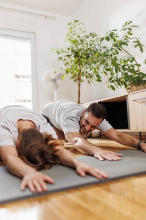 Foto de Pareja joven haciendo ejercicio juntos en casa, estirándose en la esterilla de yoga mientras hacen yoga como rutina de ejercicios matutinos - Imagen libre de derechos