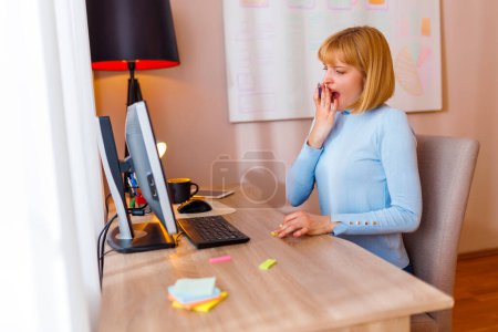 Téléchargez les photos : Femme fatiguée assise à son bureau et bâillant tout en travaillant au bureau à la maison - en image libre de droit