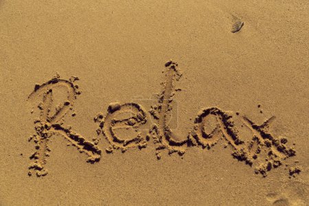 Téléchargez les photos : Word relax écrit à la main dans le sable sur la plage - en image libre de droit