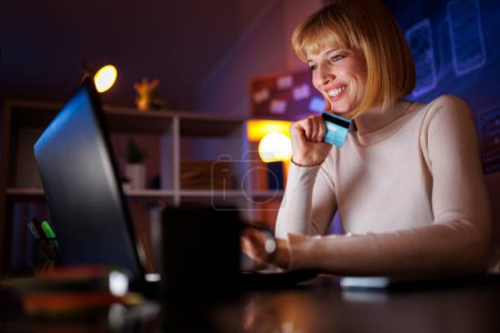 Téléchargez les photos : Femme utilisant ordinateur portable shopping en ligne en utilisant la carte de crédit tout en effectuant des paiements - en image libre de droit