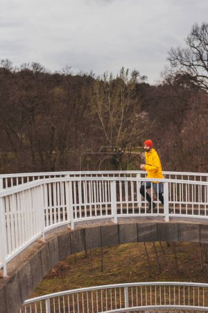 Téléchargez les photos : Homme actif en vêtements de sport faisant du jogging sur le sentier du pont par une journée d'automne nuageuse - en image libre de droit