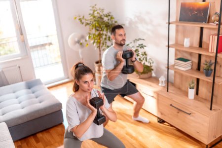 Téléchargez les photos : Couple travaillant à la maison faisant squats à l'aide d'haltères - en image libre de droit