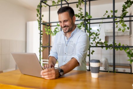 Téléchargez les photos : Développeur Web assis à son bureau à la maison en utilisant un ordinateur portable ; homme travaillant à distance de la maison - en image libre de droit