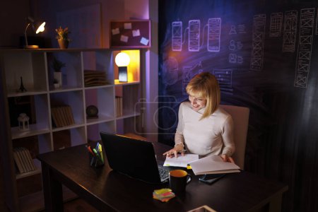 Foto de Mujer trabajando horas extras en una oficina sentada en su escritorio tarde en la noche haciendo papeleo y leyendo contratos - Imagen libre de derechos