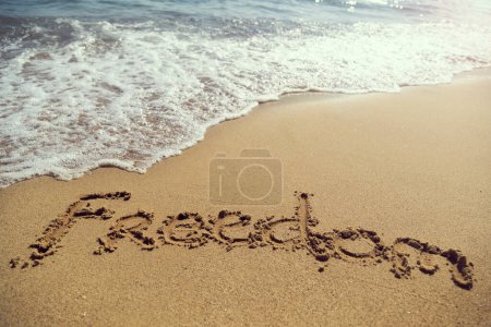 Foto de Palabra de libertad escrita a mano en arena dorada en la playa junto a la línea de flotación - Imagen libre de derechos
