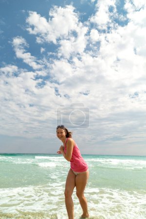 Junge glückliche Frau, die durch Wasser rennt und es bespritzt. Genuss und Freiheit im Strandurlaub